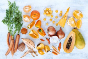 Collection of fresh orange toned vegetables and fruit raw produce on white rustic background, pumpkin butternut carrot papaya pawpaw capsicum pepper sweet potato cherry tomatoes chilli orange